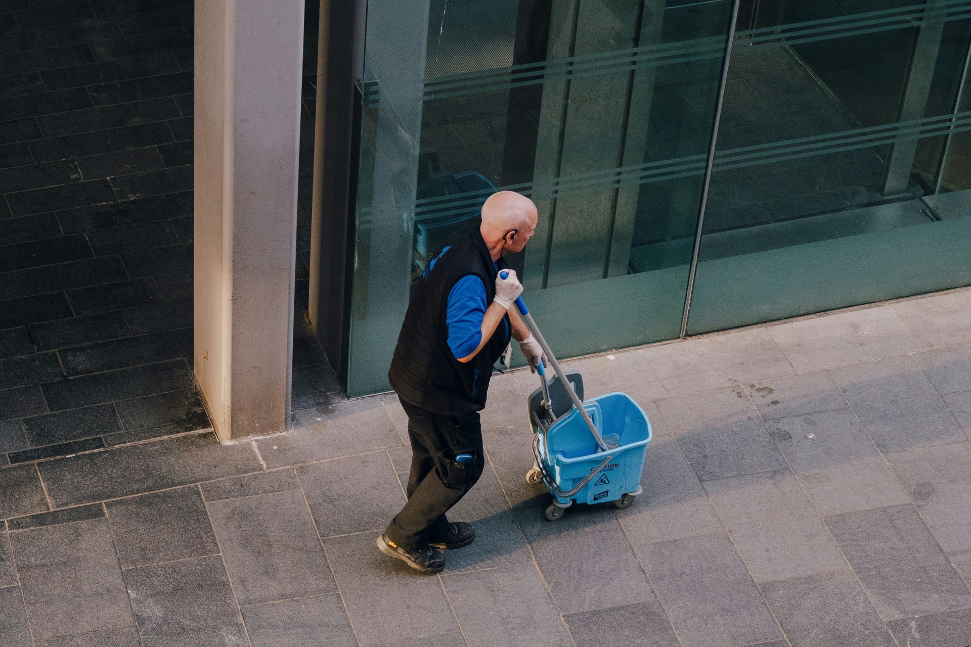 A man pulls a cleaning cart near a building.